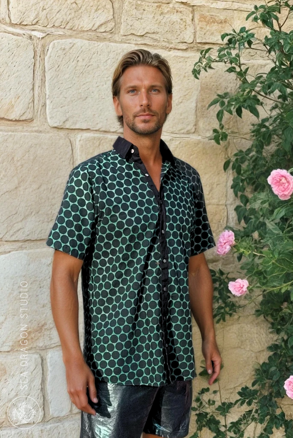 Model wearing the Green and Pleasant Land cotton-blend shirt with linen collar, standing against a stone wall with soft greenery.