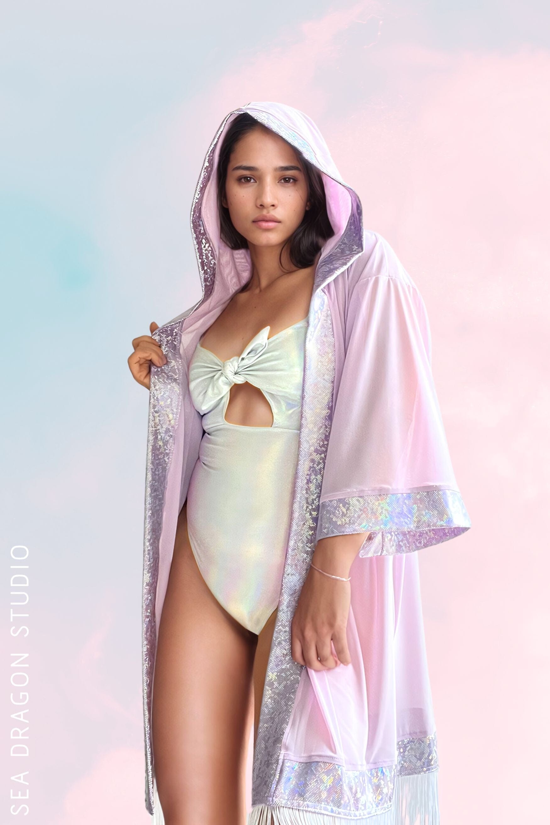 Model showcasing a pastel pink hooded kimono with holographic detailing and fringe, layered over a light mint holographic one-piece. The look is perfect for festival fashion, combining elegance with a vibrant, futuristic style