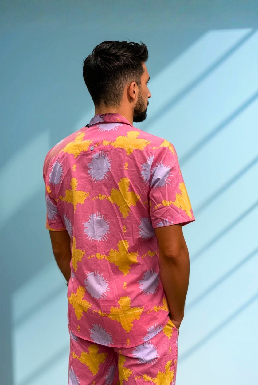 Back view of the Tropic Drift pink summer shirt and shorts set, worn by model against a blue wall.