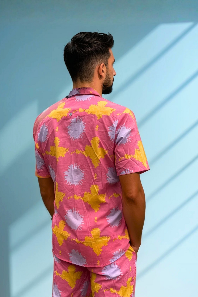 Back view of the Tropic Drift pink summer shirt and shorts set, worn by model against a blue wall.