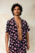 Model wearing the Malibu Barbie Palm Party short-sleeve rayon shirt in pink palm print, standing against a light textured wall.