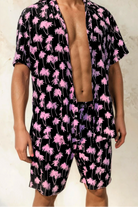 Model wearing the Malibu Barbie Palm Party rayon shorts in pink palm print, standing against a light textured wall.