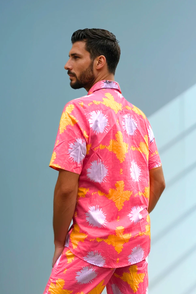 Model standing in a relaxed pose facing the wall wearing Sea Dragon Studio’s Tropic Drift pink summer matching set against a sky-blue wall.